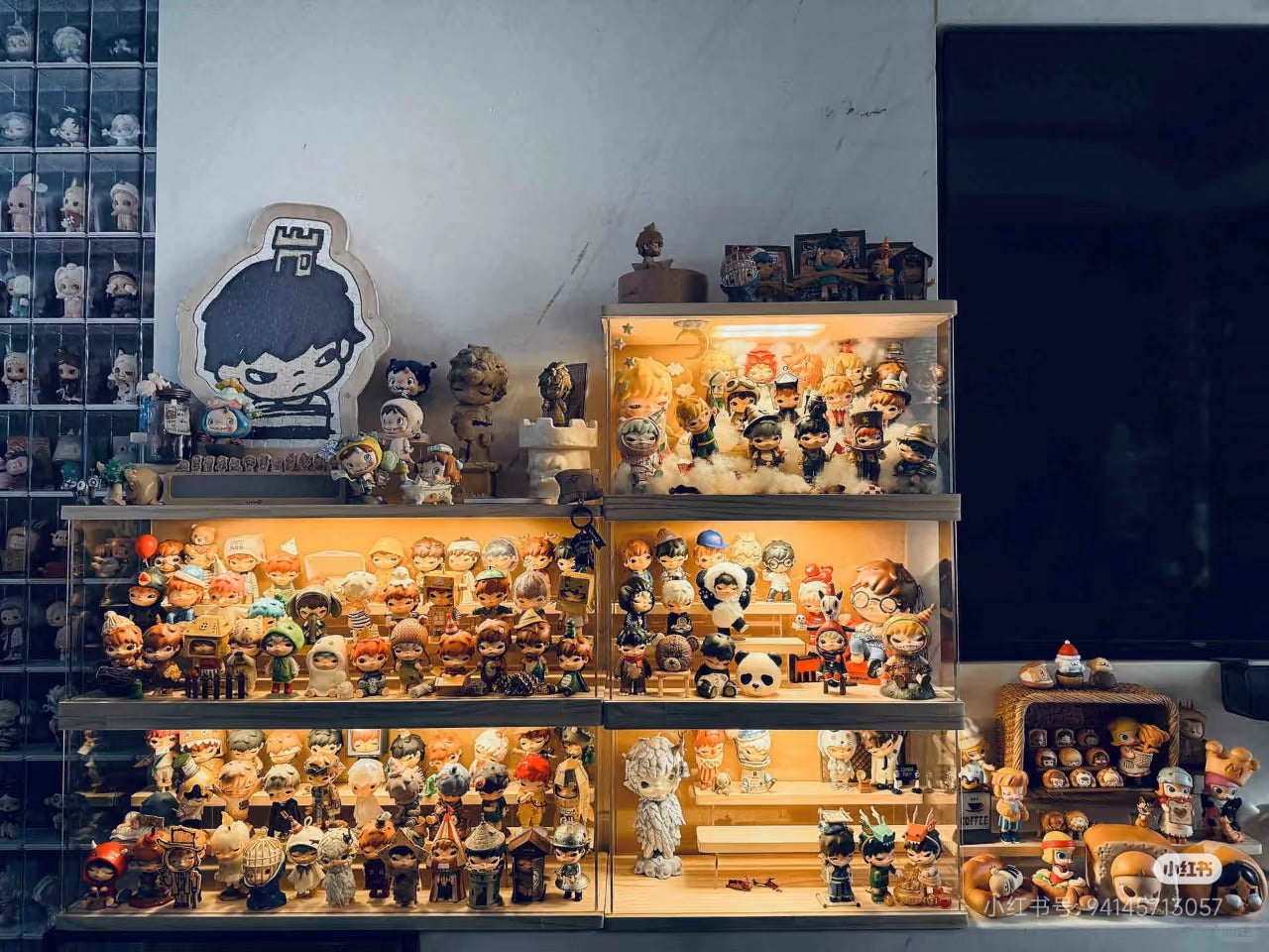 A multi-tiered, backlit shelf filled with numerous vinyl figures and collectibles against a white wall, including Hirono and Molly series from POP MART.