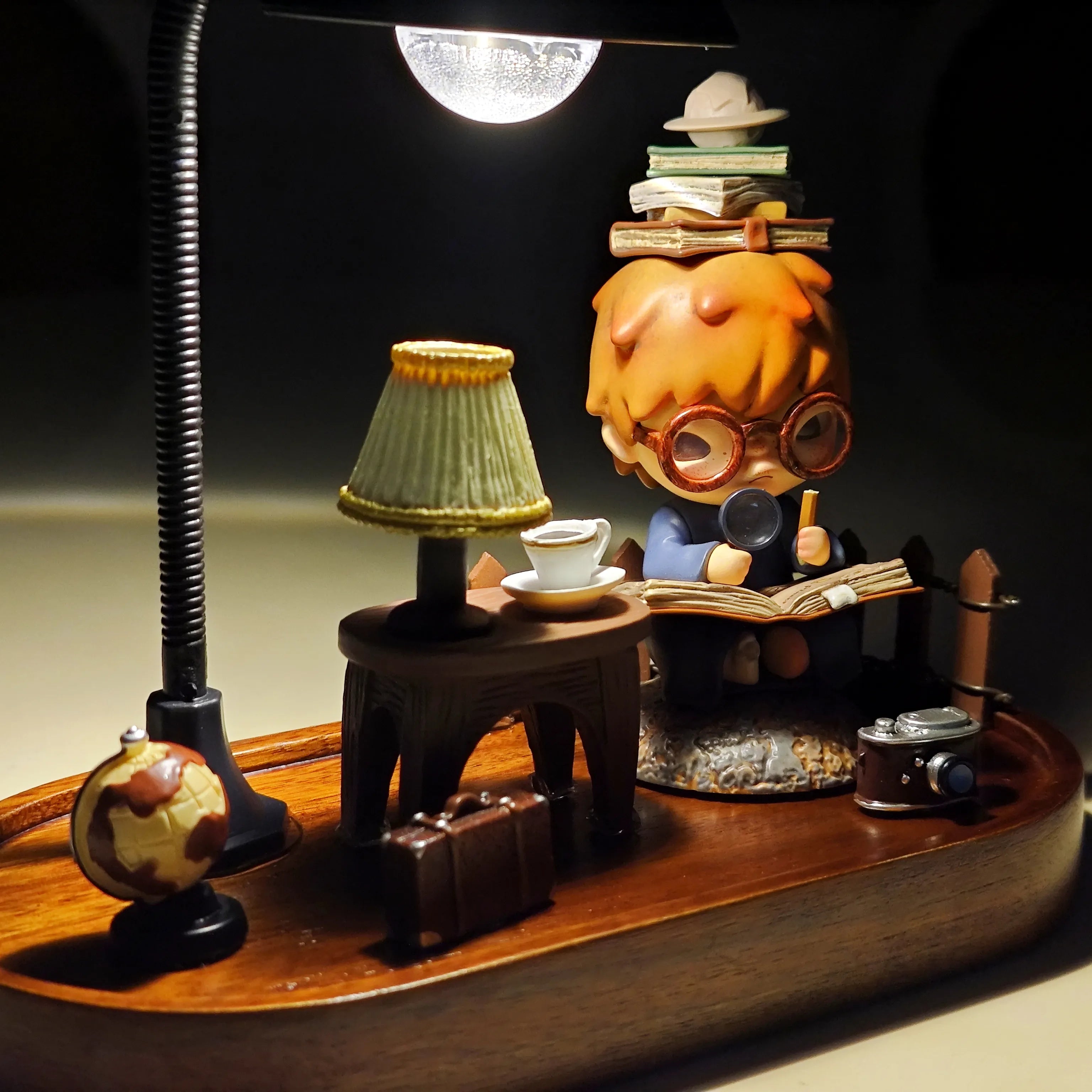 Complete Hirono the Geographer diorama featuring a globe, lamp, suitcase, camera, and figure reading a book under warm lamplight.