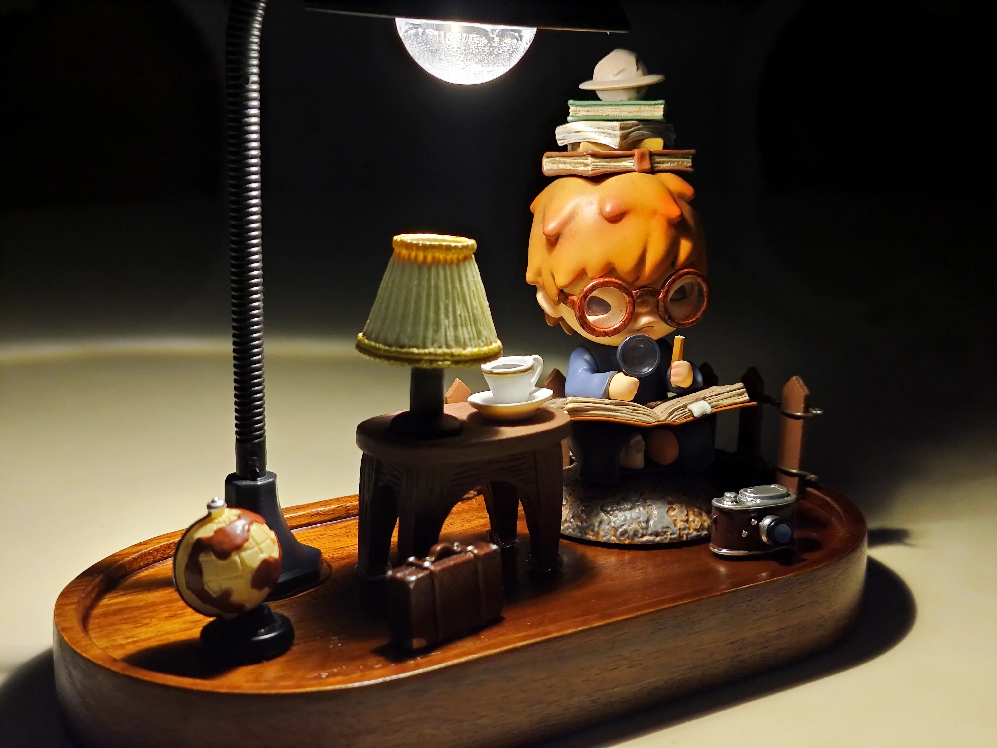 Complete Hirono the Geographer diorama featuring a globe, lamp, suitcase, camera, and figure reading a book under warm lamplight.