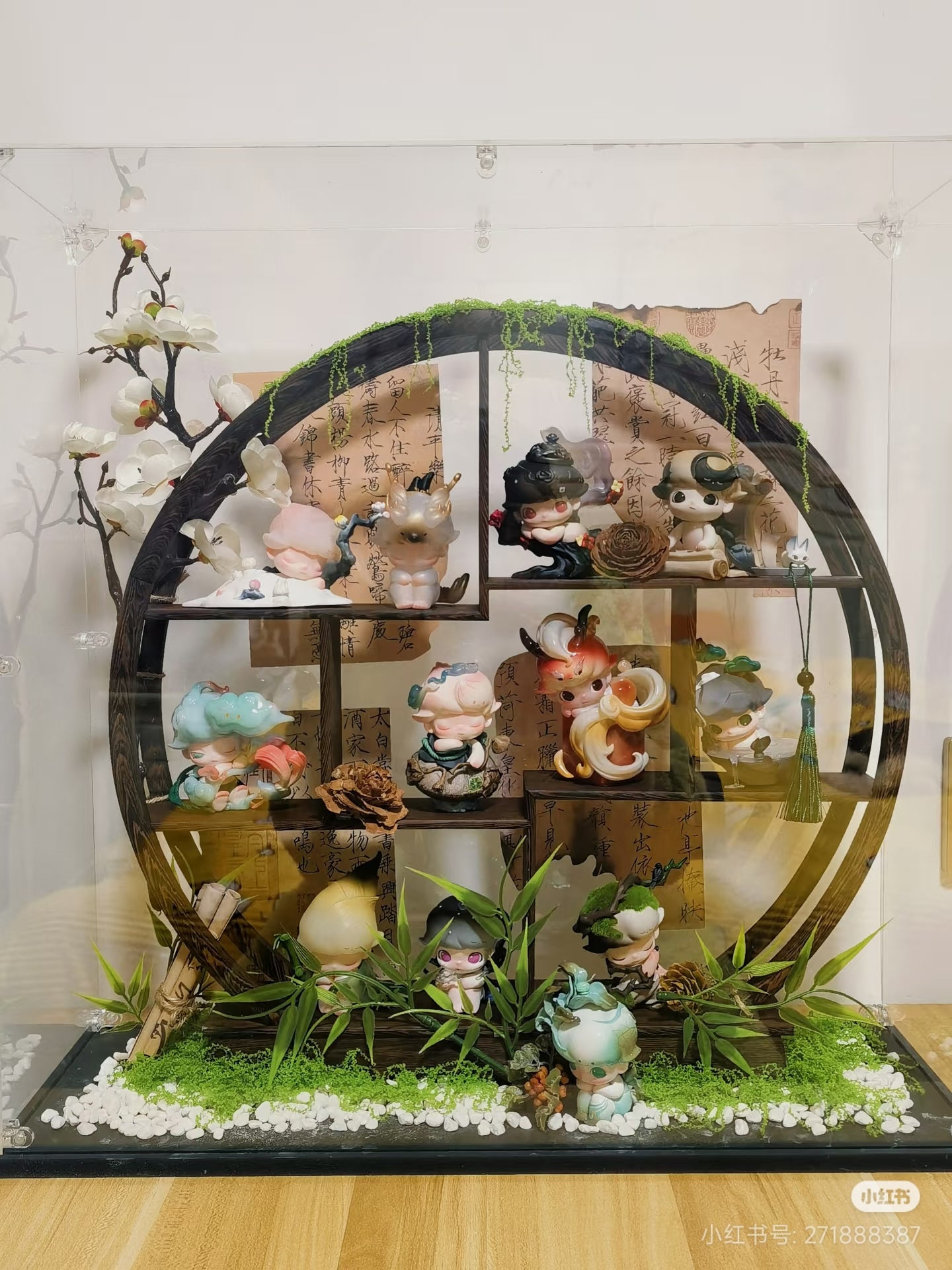 A decorative circular shelf enclosed in an acrylic case, featuring nature-inspired elements and collectible DIMOO Stories in the Cup figures with a traditional Asian flair. 