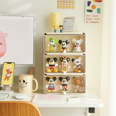 Three stacked cream-colored drawer boxes displaying collectible Mickey figures on a bright modern workspace