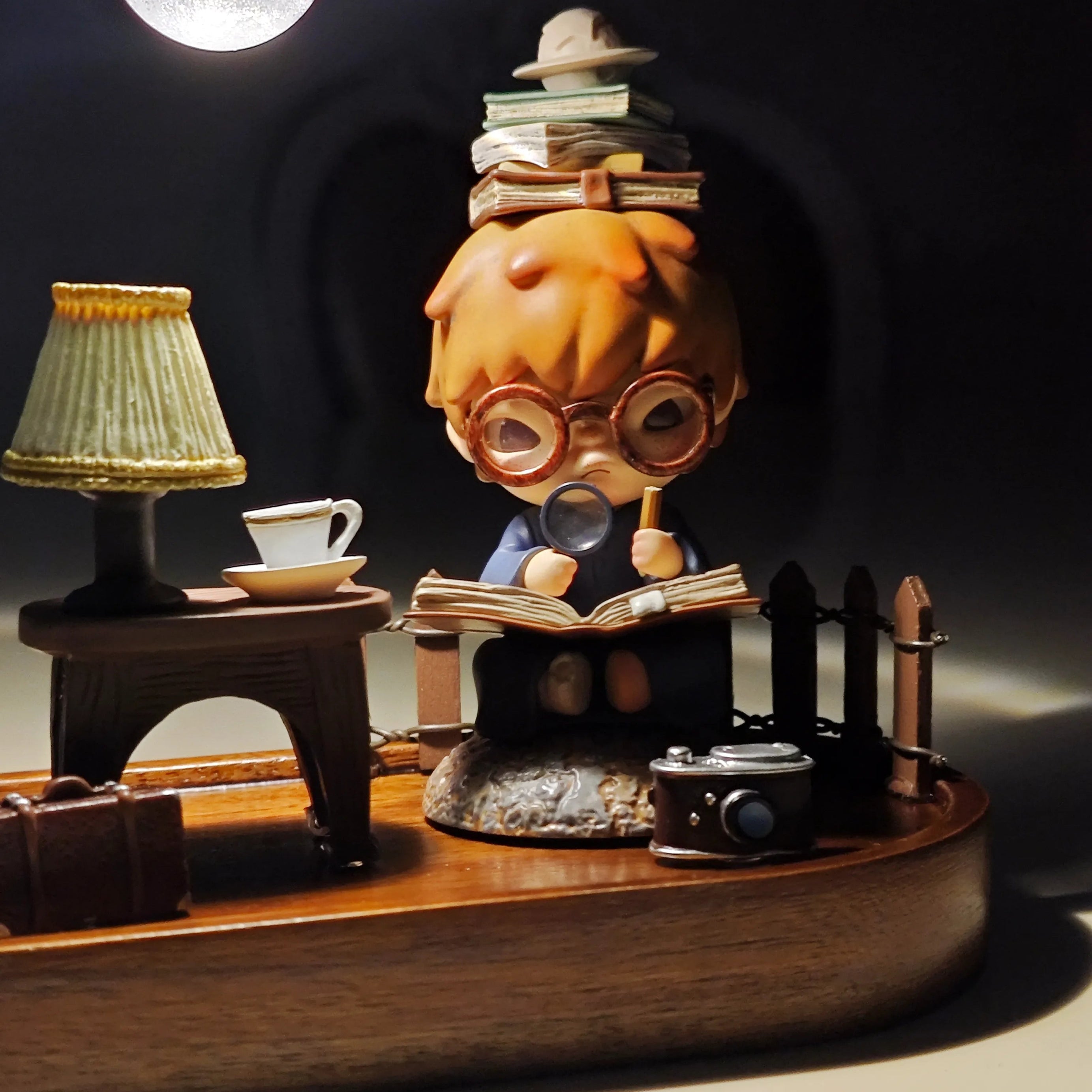 Hirono the Geographer figure closely reading with a magnifying glass and stacked books under overhead lamp.