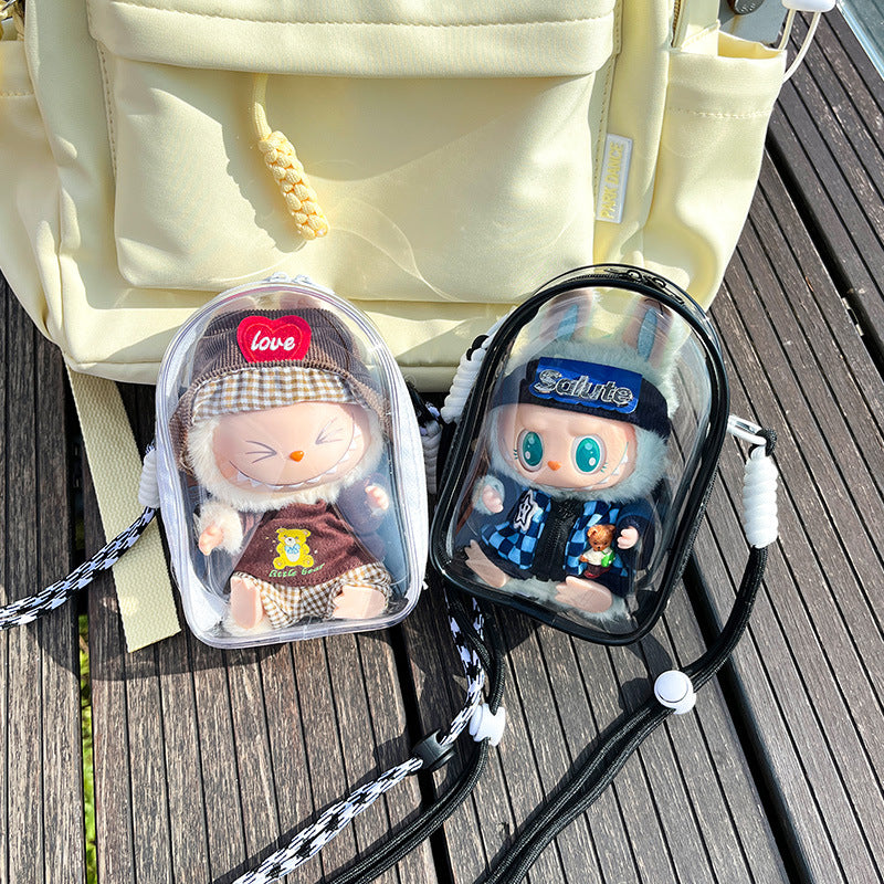 Two transparent PVC display bags placed on a wooden surface next to a yellow backpack. The bags feature Labubu figures in brown and blue outfits, with black and white straps, respectively. Great for collectors.