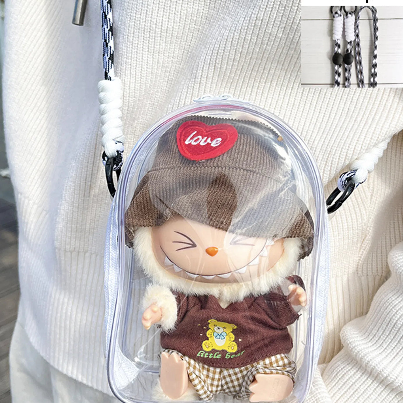 Transparent PVC display bag with a white strap, featuring a Labubu collectible figure dressed in a brown sweater with a bear motif and a matching brown hat. This practical and playful bag is crafted for Pop Mart figure enthusiasts and protects against dust and moisture.