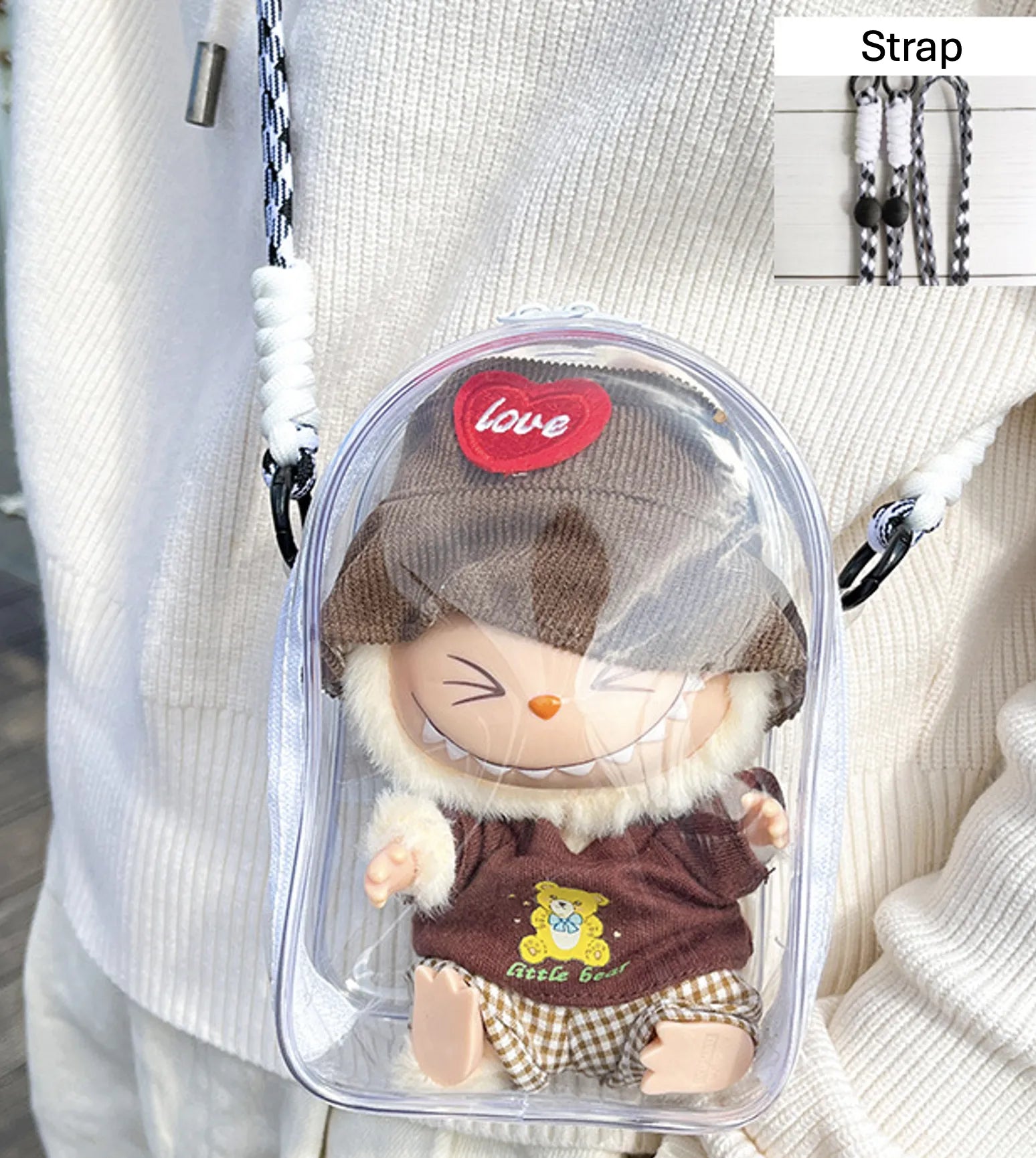 Transparent PVC display bag with a white strap, featuring a Labubu collectible figure dressed in a brown sweater with a bear motif and a matching brown hat. This practical and playful bag is crafted for Pop Mart figure enthusiasts and protects against dust and moisture.