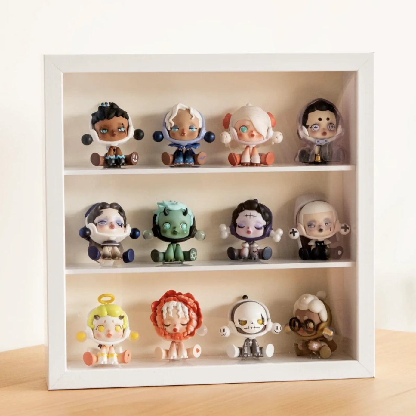 A squared white wooden display case from Fig Palace with three layers,featuring a collection of designed Skullpanda figures from Popmart, each with distinct colors and styles,neatly arranged for display.