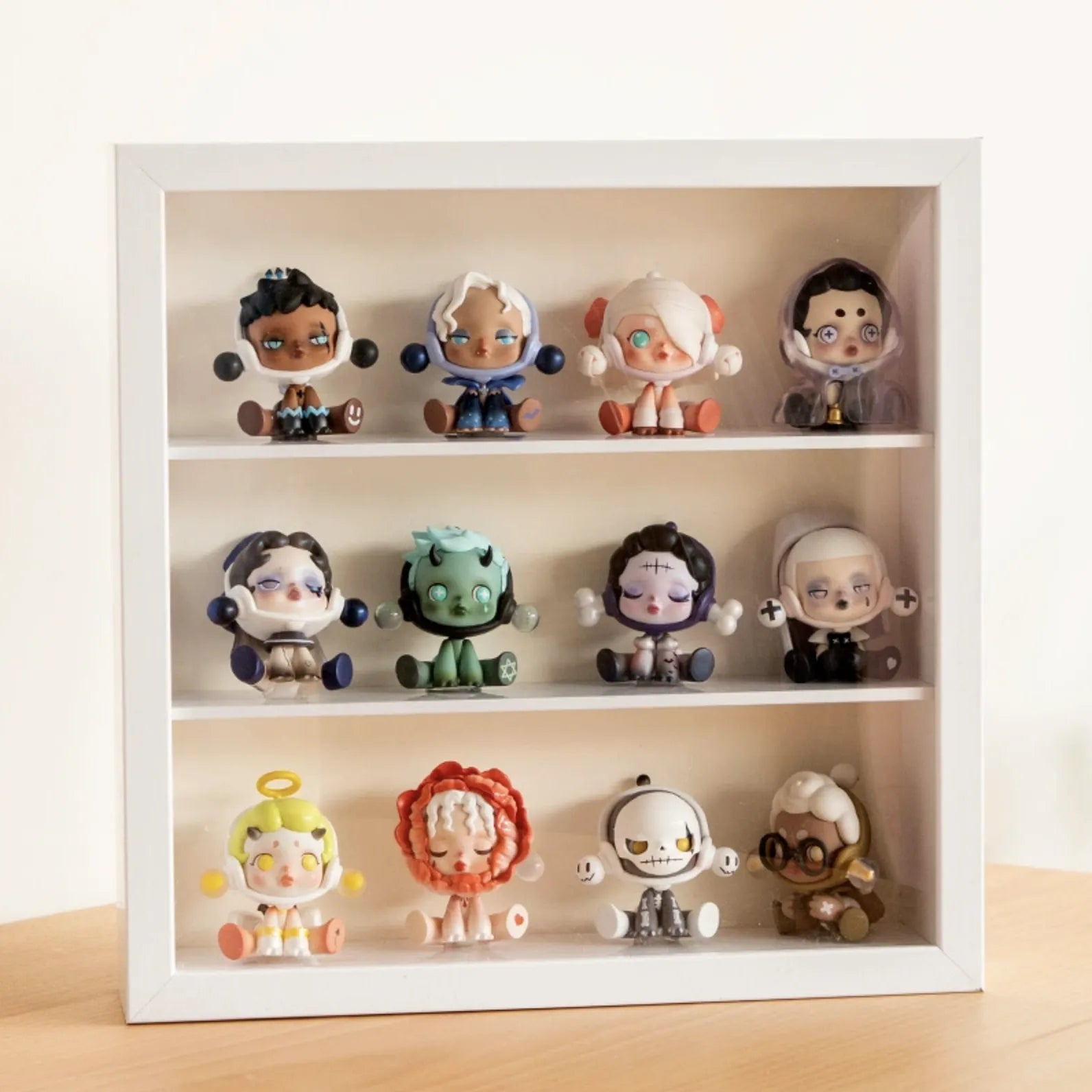 A squared white wooden display case from Fig Palace with three layers,featuring a collection of designed Skullpanda figures from Popmart, each with distinct colors and styles,neatly arranged for display.